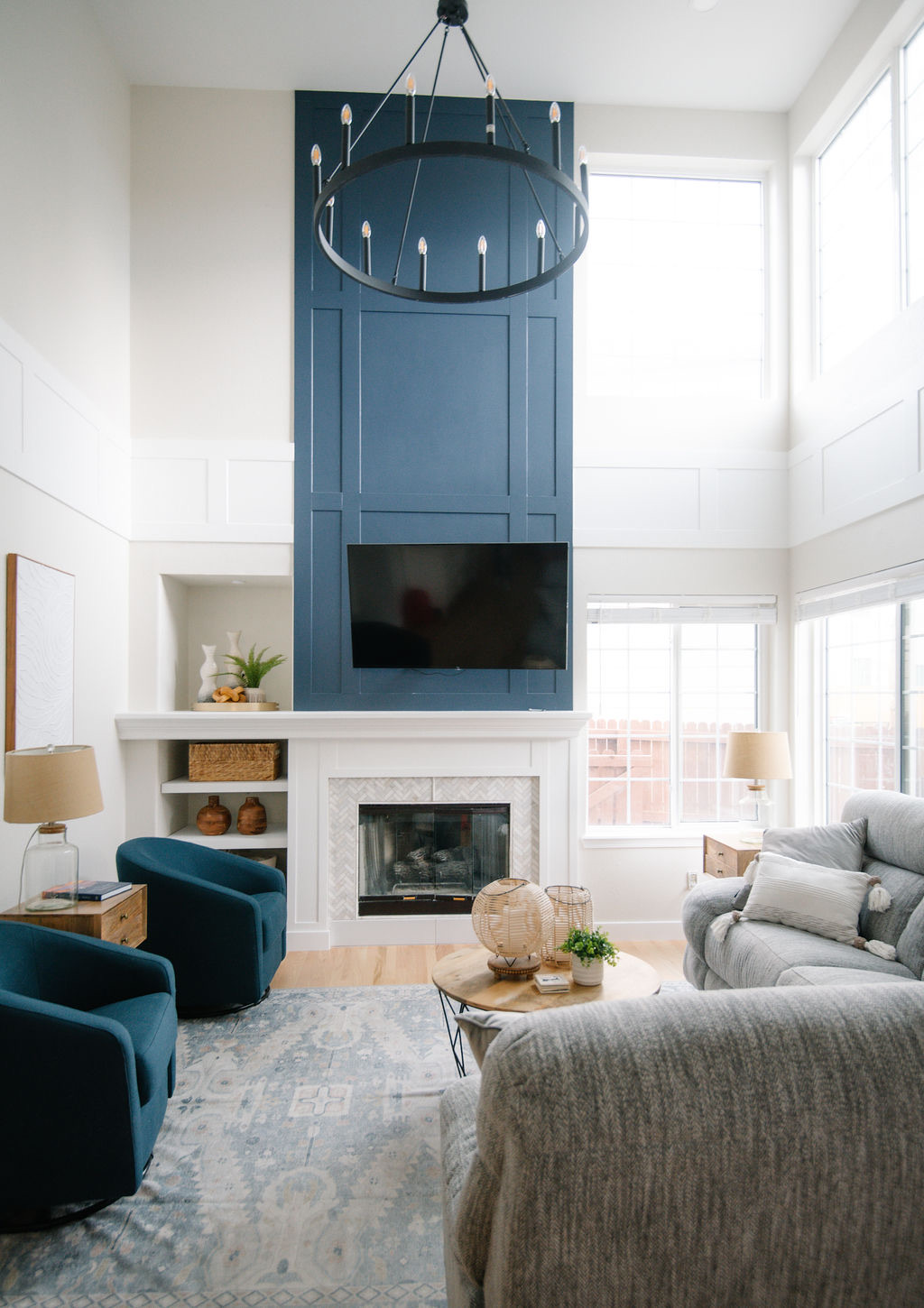 Two-story family room with navy shiplap fireplace, round chandelier, and teal swivel chairs — Stonegate main floor renovation in Parker, Colorado