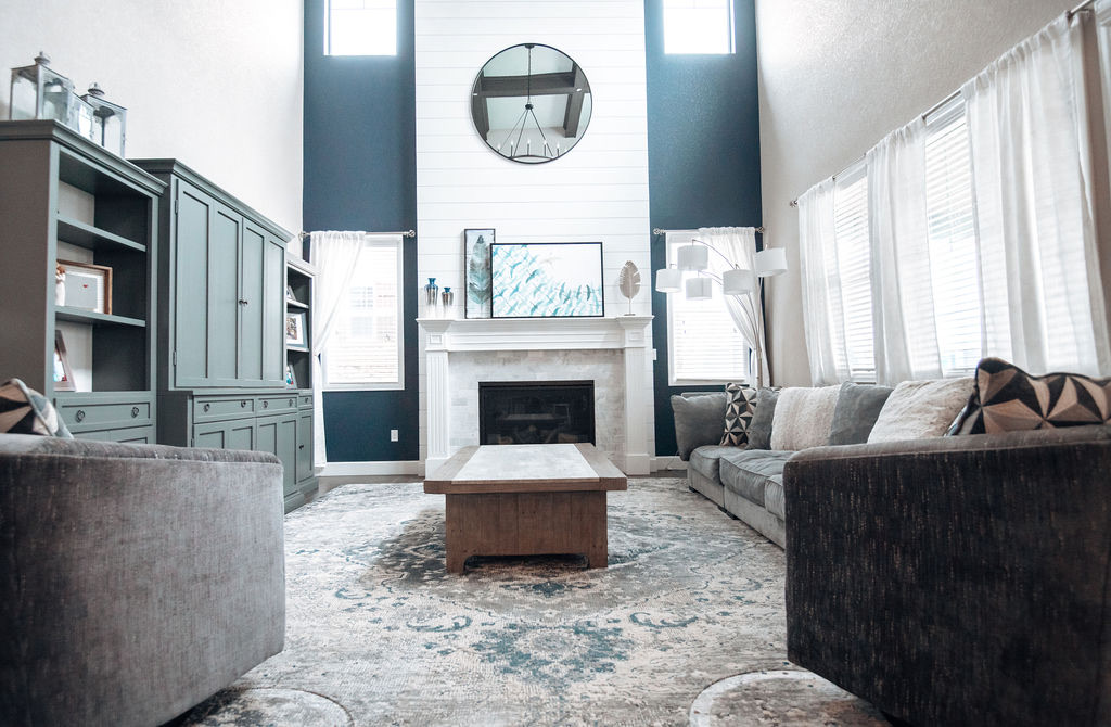 Double-height family room with faux wood beams, shiplap fireplace wall, and gray sectional — Blackstone family room renovation in Aurora, Colorado