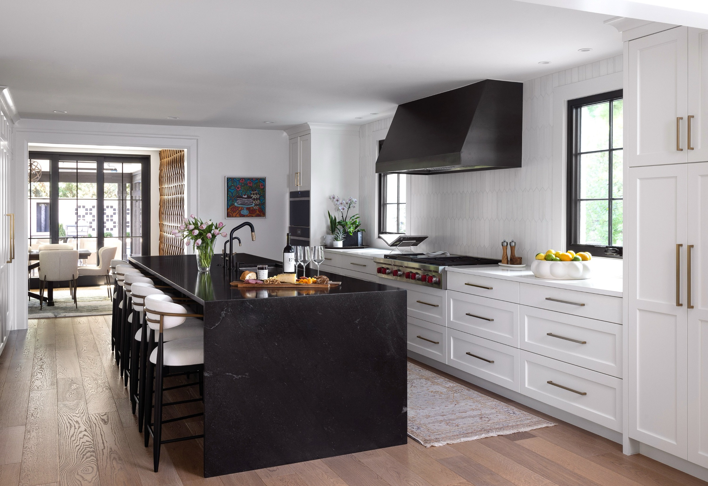 photo of modern kitchen with white perimeter cabinets, black metal freestanding hood and black waterfall kitchen island with gold hardware.