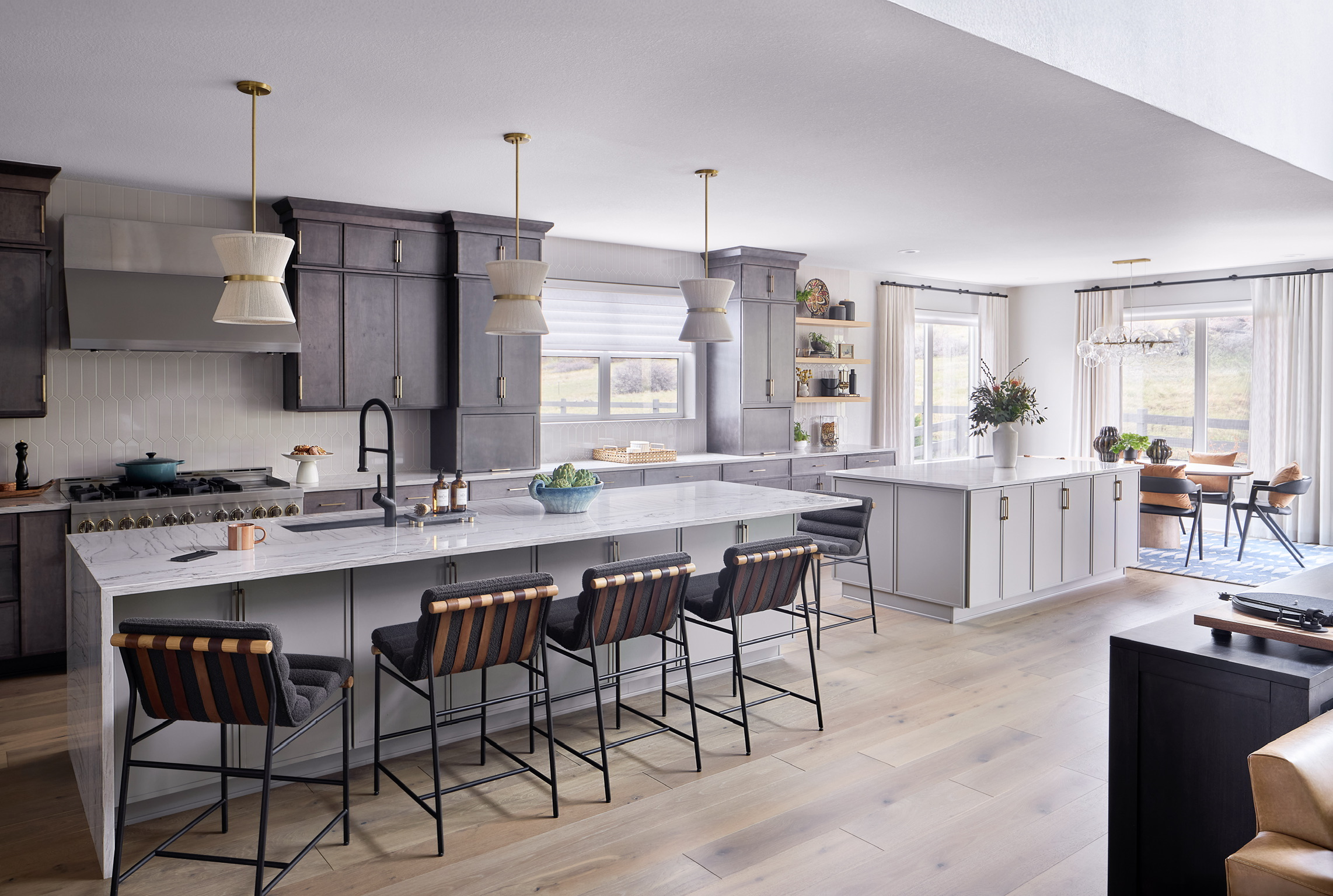 Castle Pines kitchen with double islands, dark cabinetry, marble-look countertops, pendant lights, breakfast nook, and open living room.
