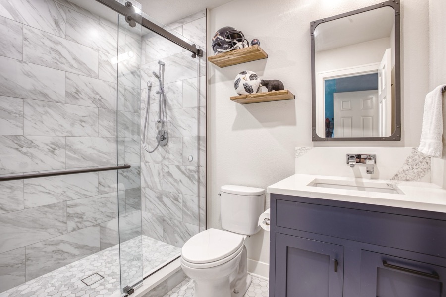 Guest bath with sliding glass shower and navy vanity — Fulton Street whole house renovation in Greenwood Village