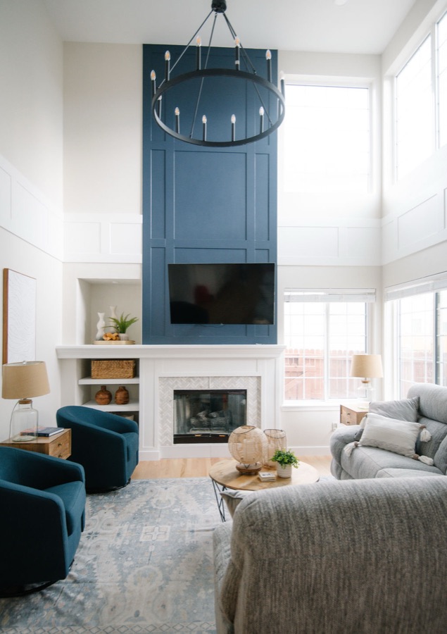 Two-story family room with navy shiplap fireplace, round chandelier, and teal swivel chairs — Stonegate main floor renovation in Parker, Colorado