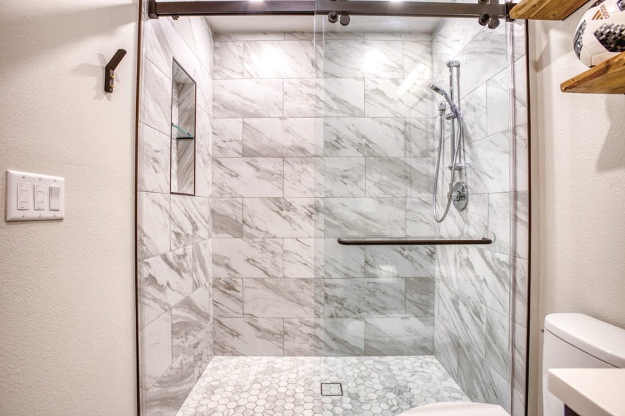 Marble-look shower with hex-tile floor and floating shelves — Fulton Street whole house renovation in Greenwood Village
