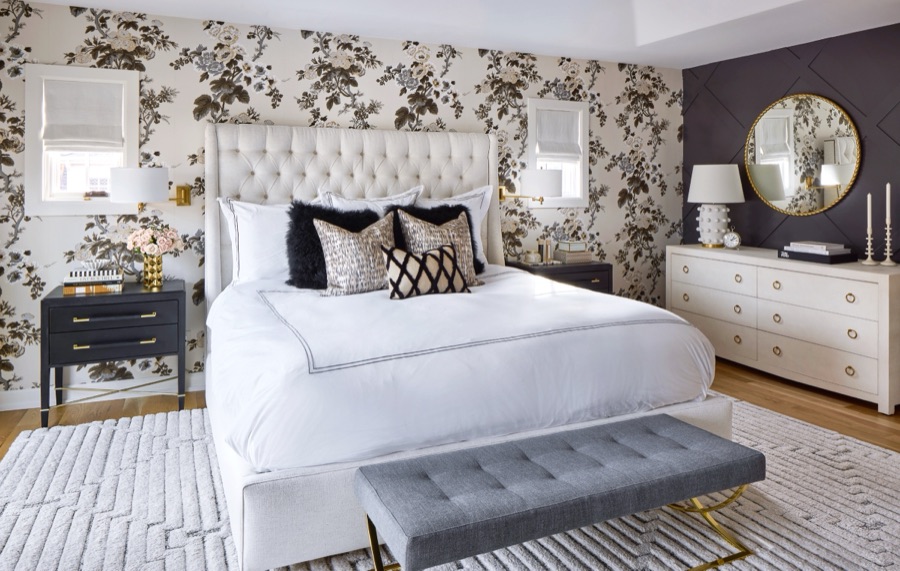beautiful bedroom with white tufted king bed, floral wallpaper behind, black x paneling behind white linen dresser with gold rings. luxury decor, linens and window coverings