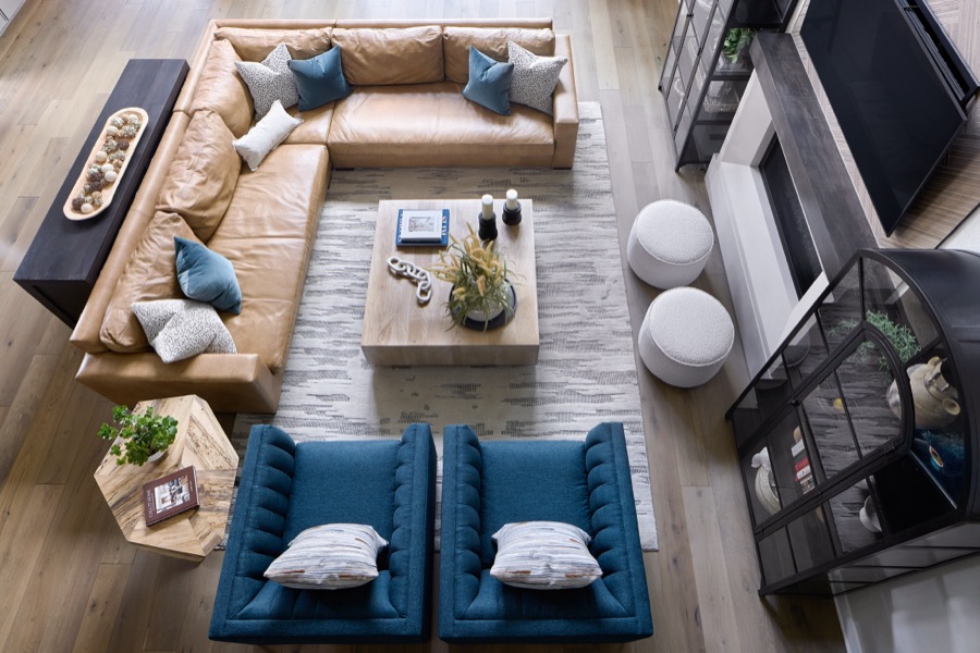 Overhead view of living room with tan leather sectional, blue lounge chairs, fireplace, coffee table, and arched display cabinet.
