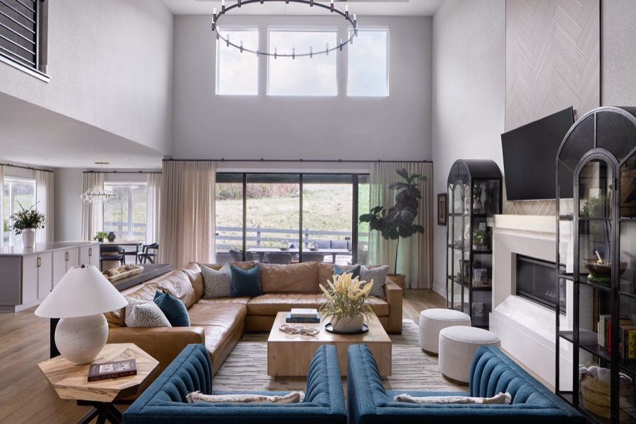 Large Castle Pines living room with tan leather sectional, blue chairs, arched display cabinets, fireplace, and open kitchen.